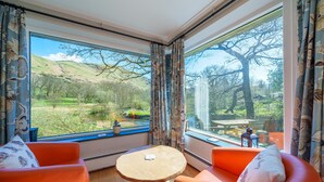 Une pièce avec deux fauteuils orange, une petite table ronde et une vue sur un paysage verdoyant, visible à travers de grandes fenêtres.