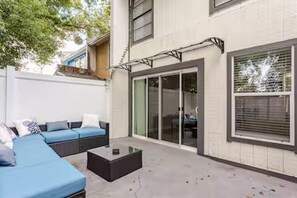 Un espace de vie extérieur moderne, doté d’un canapé modulable, d’une table basse et d’une porte-fenêtre coulissante donnant sur un patio.