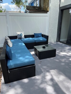 A sectional sofa with blue cushions and a glass coffee table in an outdoor patio area.