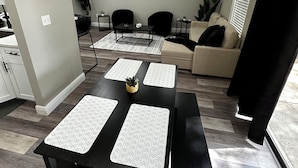 Un comedor con una mesa negra y cuatro individuales a juego, un sofá negro y un sofá beige al fondo.