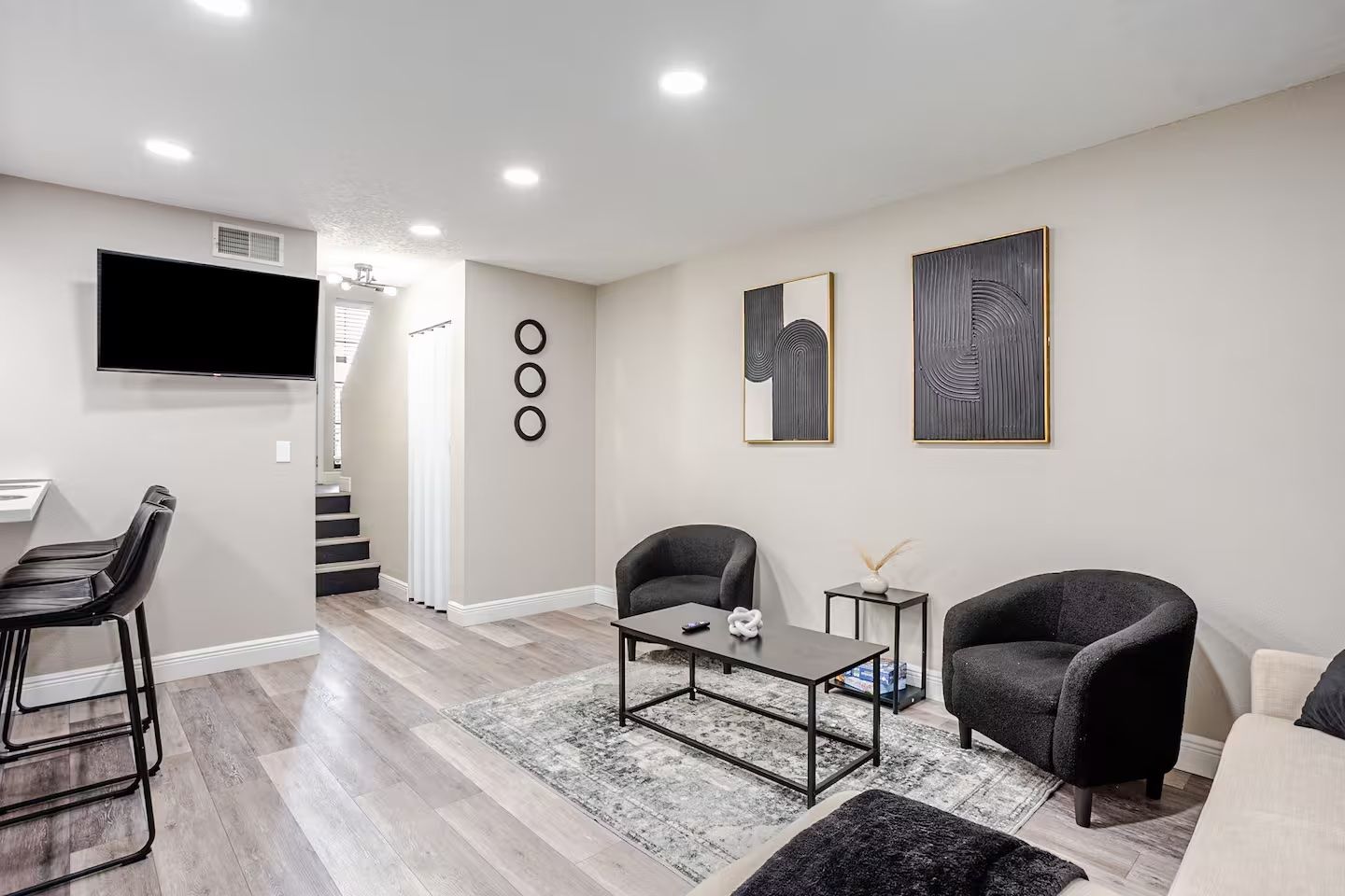 Een moderne woonkamer met een flatscreen televisie, twee fauteuils, een salontafel en een trap naar een hoger niveau.