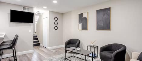 Een moderne woonkamer met een flatscreen televisie, twee fauteuils, een salontafel en een trap naar een hoger niveau.