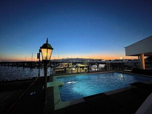 A pool area with a view of boats and a sunset in the background.