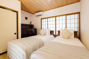 Two single beds with striped bedding and matching pillows, set against a traditional Japanese backdrop with a shoji screen window and dark dresser.