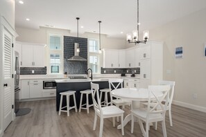 Eine moderne Küche mit weißen Schränken, einer schwarzen Spritzschutzwand und einer zentralen Kochinsel mit Hockern.