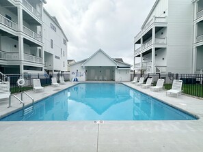 Ein Schwimmbecken mit einer 1,50 Meter Tiefenmarkierung, umgeben von weißen Gebäuden mit Balkonen und Liegestühlen.