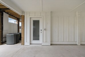 Una puerta blanca y limpia con un ventanal, un equipo de aire acondicionado pequeño y una pared lisa.