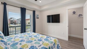 Ein Schlafzimmer mit einem Bett, einem Deckenventilator, einem Fernseher und einem Balkon mit Vorhängen.