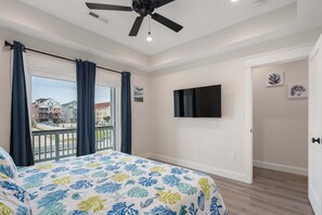 Ein Schlafzimmer mit einem Bett, einem Deckenventilator, einem Fernseher und einem Balkon mit Vorhängen.