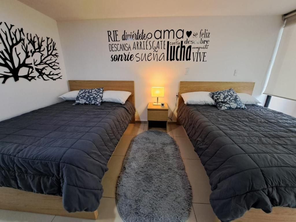 Habitación doble con cama, alfombra, dos mesitas de noche y una pared decorada con un dibujo de un árbol y frases motivadoras.