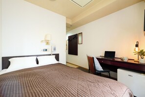 Ein Hotelzimmer mit Bett, Schreibtisch, Stuhl, Lampe, Telefon und kleinem Kühlschrank.