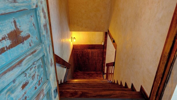 A wooden staircase with a handrail, a light fixture at the top, and a blue door with peeling paint.
