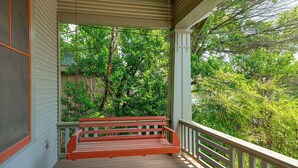 A porch with a wooden bench, surrounded by greenery and a white railing.