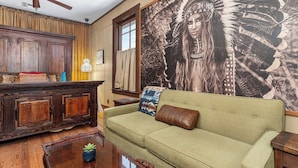 A living room with a green sofa, wooden cabinet, and a large wall mural.