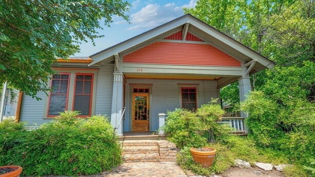 A two-story house with a red roof and white trim, a front porch, and a brick pathway leading to the entrance.