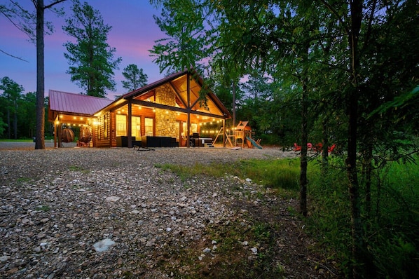 A log cabin with a stone foundation, wooden exterior, and a gravel driveway.