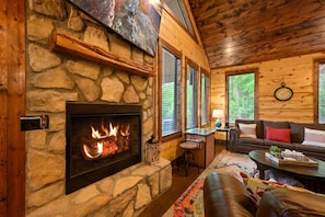 Une cheminée en pierre avec un feu de bois, un plafond en bois, un canapé et un coin bar.