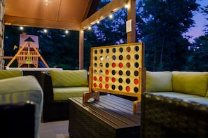 An outdoor seating area with a wooden table, green cushioned sofas, and a wooden board game.