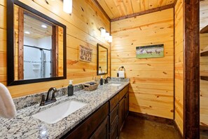 Une salle de bain rustique, avec des murs en bois, Ă©quipĂ©e de deux lavabos, dâun grand miroir et dâun porte-serviettes.