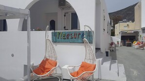 Un edificio blanco con un letrero que dice "Pleasure" y dos sillas de mimbre blancas con cojines anaranjados.