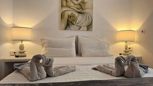 Habitación de hotel con una cama, dos lámparas de noche, un cuadro en la pared y toallas dispuestas sobre la cama.