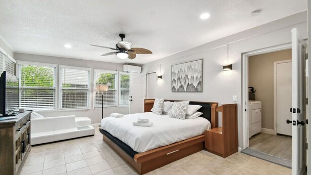 A modern bedroom with a large bed, a ceiling fan, and a view of the outdoors through large windows. - Red Royalty Pool, King Bed, Yard (Tampa)