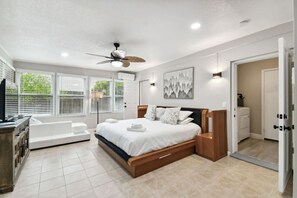 A modern bedroom with a large bed, a ceiling fan, and a view of the outdoors through large windows. - Red Royalty Pool, King Bed, Yard (Tampa)