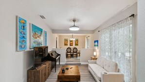 A living room with a sofa, coffee table, TV, and artwork on the wall. - Red Royalty Pool, King Bed, Yard (Tampa)
