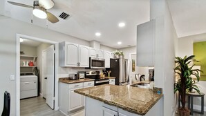 A modern kitchen with white cabinets, granite countertops, stainless steel appliances, and a ceiling fan. - Red Royalty Pool, King Bed, Yard (Tampa)