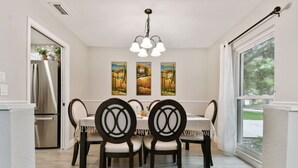 A dining area with a white table, black chairs, and three paintings on the wall. - Red Royalty Pool, King Bed, Yard (Tampa)