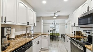 A modern kitchen with white cabinets, granite countertops, a dishwasher, a microwave, and a stove. - Red Royalty Pool, King Bed, Yard (Tampa)