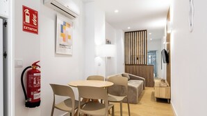 A modern hotel room with a dining area, a sofa, a lamp, a fire extinguisher, and a wooden partition.