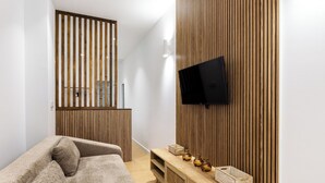 A modern room with a sofa, a TV mounted on a wooden wall, and a small wooden console table with decorative items.