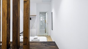 A modern hotel hallway with a wooden floor, a white wall, and a glass shower area.