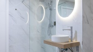 Et moderne badeværelse med en glasafskærmet brusekabine, et rundt spejl og en trækommode med en hvid vask.