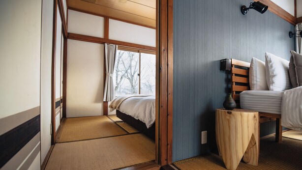 A traditional Japanese-style room with tatami flooring, a wooden bed, and a view of trees through a window.