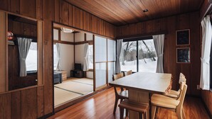 A traditional Japanese room with tatami flooring, a wooden dining table, and sliding doors leading to a view of a snowy landscape.