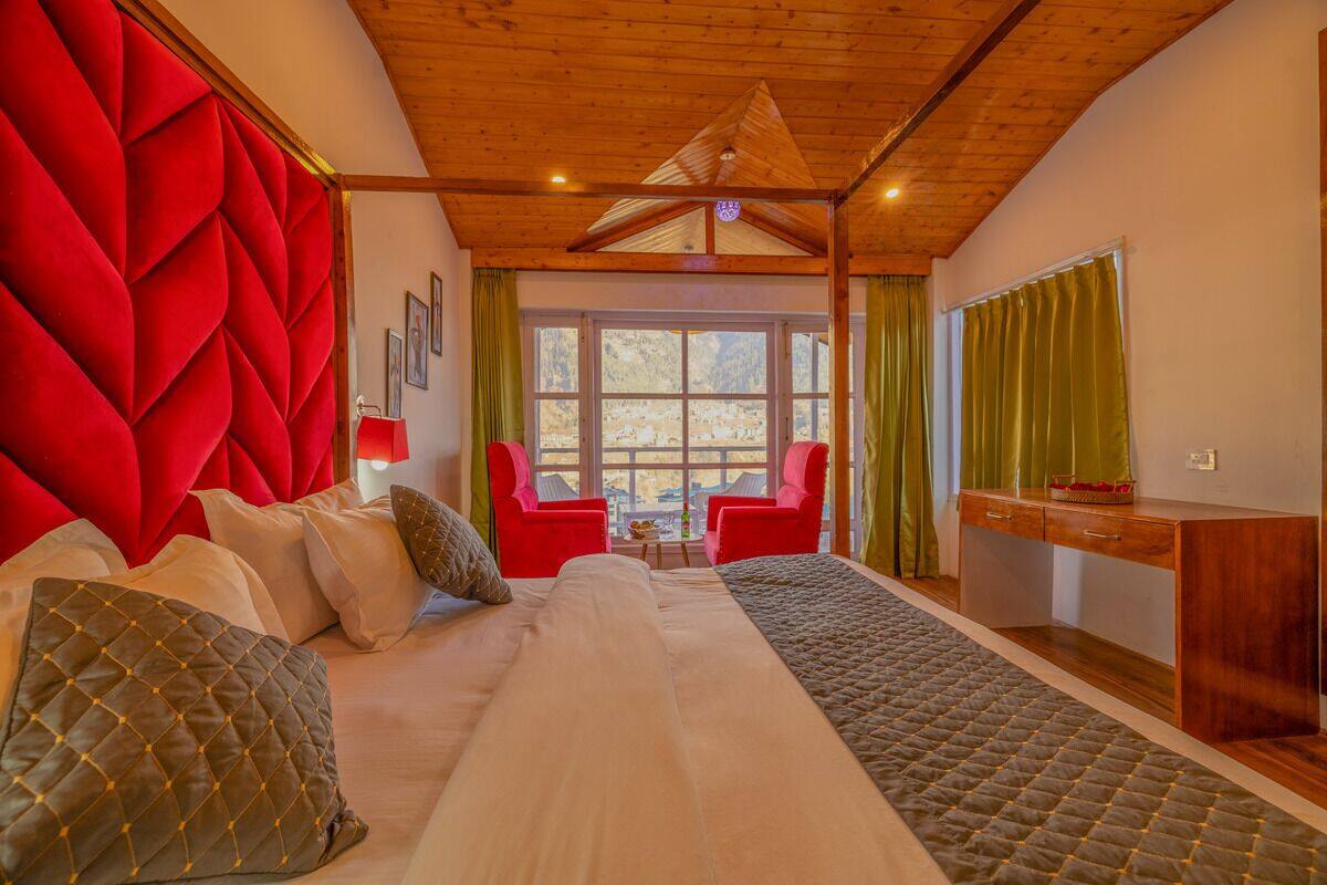 A bedroom with a large bed, red upholstered headboard, wooden ceiling, and a view of the outdoors through a window.