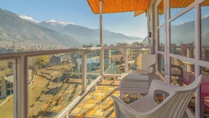 A balcony with a view of a mountainous landscape, white wicker chairs, and a wooden ceiling. - Hyacinth Hotel (Manali)