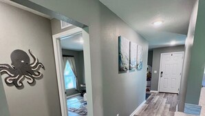 A spacious hallway with a wooden floor, a black octopus wall decoration, and a door leading to another room.
