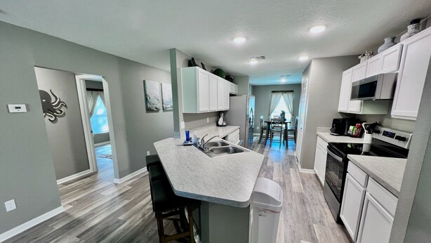 A modern kitchen with a central island, bar stools, a sink, and built-in appliances.