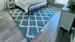 A bedroom with a bed, nightstands, a desk, a window with curtains, and a patterned rug.