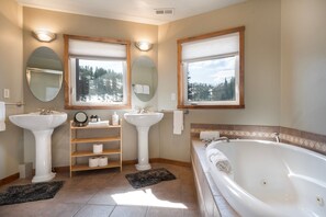 Un baño con dos lavamanos, una bañera y una ventana que da a árboles.
