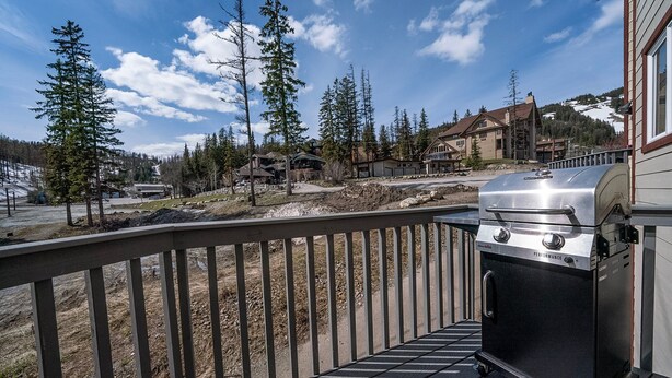 A barbecue grill on a deck with a view of a mountainous area and several buildings.