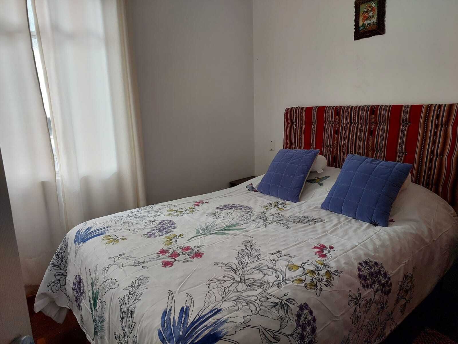 A bed with floral bedding, two pillows, a striped headboard, and a small framed picture on the wall.