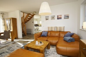 Un salon moderne avec un canapé en cuir marron, une table basse en bois et un escalier menant à l’étage supérieur.