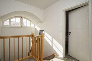 Un escalier avec des rampes en bois, une porte blanche et une fenêtre donnant sur les bâtiments environnants.