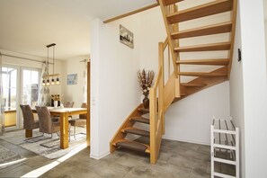 Ein modernes Interieur mit einer Holztreppe, einem Essbereich mit Tisch und Stühlen und Blick durch eine Glastür.