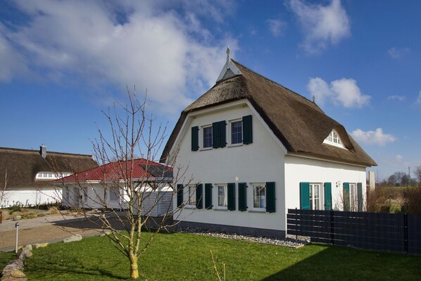 Une maison blanche avec un toit de chaume, des volets verts et une pelouse bien entretenue.