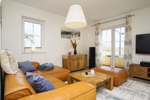 Un salon moderne avec un ensemble de canapés, une table basse en bois, un téléviseur et une grande fenêtre avec des rideaux.